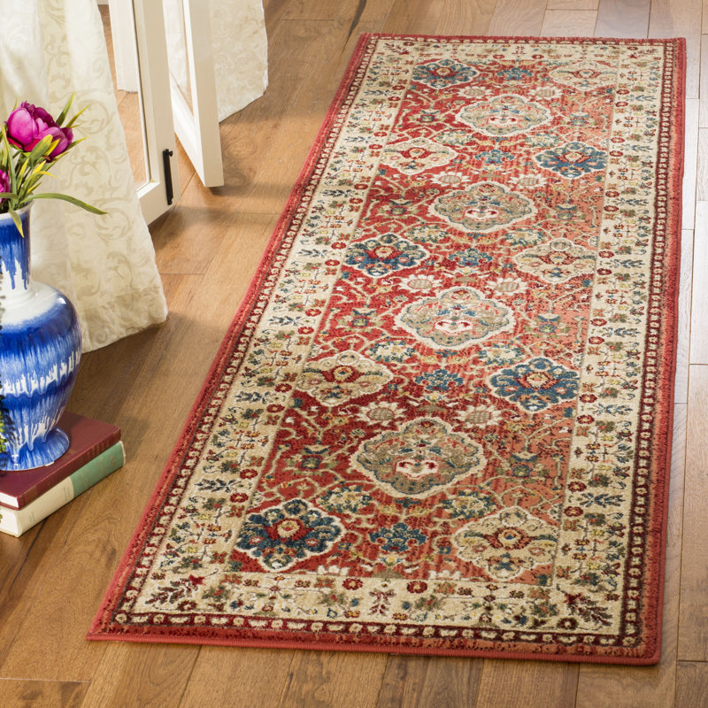 Runner rug in red, blue, and cream with a traditional floral medallion pattern on a hardwood floor.