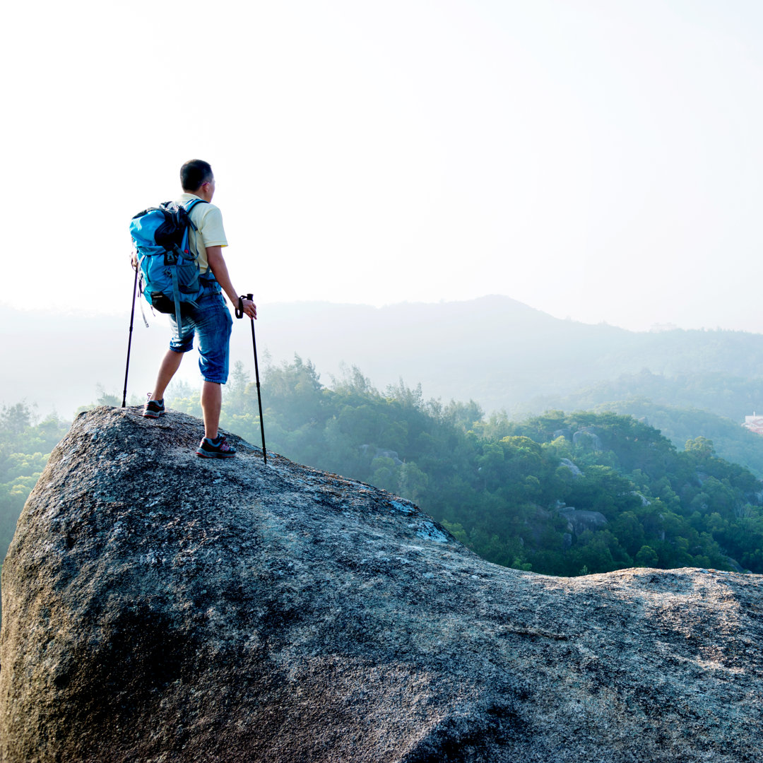 Männlicher Wanderer, der auf einem Felsen steht von Baona - Druck auf Leinwand ohne Rahmen