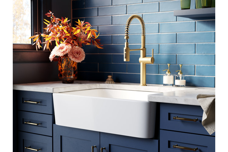 how to install a farmhouse sink in a monochromatic blue modern kitchen with blue backsplash tiles and cabinets and a white apron sink with gold faucet and sink set