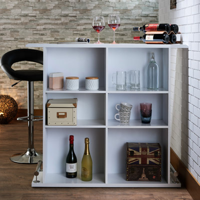 Table de bar blanche laquée brillante avec 6 compartiments de rangement ouverts, plateau fixe en bois, repose-pieds en métal sur le piètement avant, profondeur 41,5 cm, largeur 120 cm, poids 39 kg. Finition de table, cadre et supports inclus.