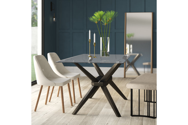 Modern dining table with a glass tabletop and black splayed table legs.
