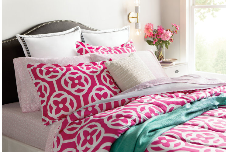Bright pink geometric comforter on a bed with coordinating sheets, shams, and pillow cases.