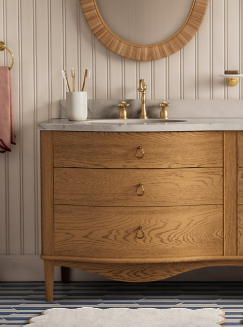 Bathroom vanity with three drawers, gold hardware, and round mirror.
