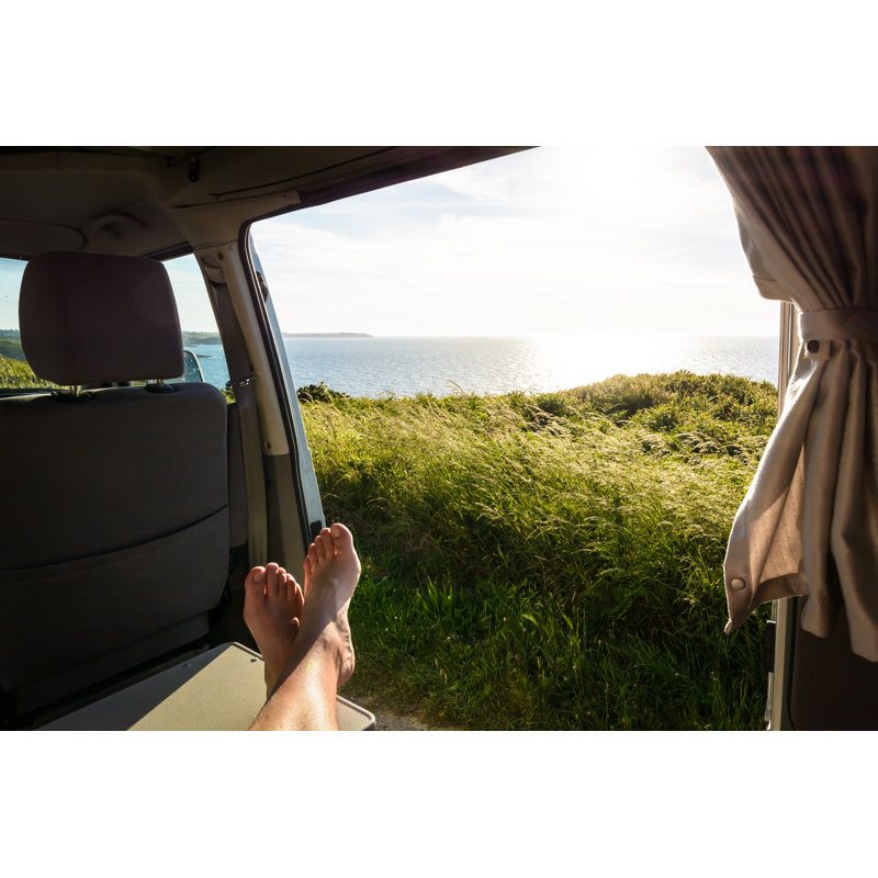 First-person View Of A Barefoot Man Relaxing Inside A Camper Van And Enjoying The View Over The Sea At Sunset by Olrat - Wrapped Canvas Print