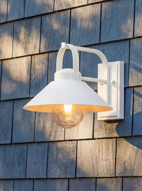 Lit white outdoor barn light on a gray shingle wall.