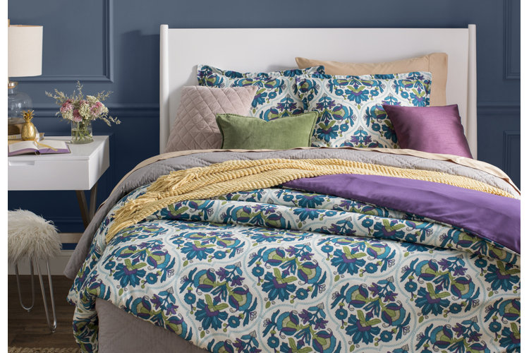 bed layered with a teal, green, and purple patterned bedding set and pink, green, and purple throw pillows