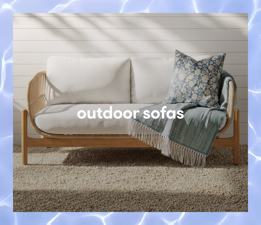 A modern wooden outdoor sofa with white cushions, a blue patterned pillow, and a fringed throw blanket.