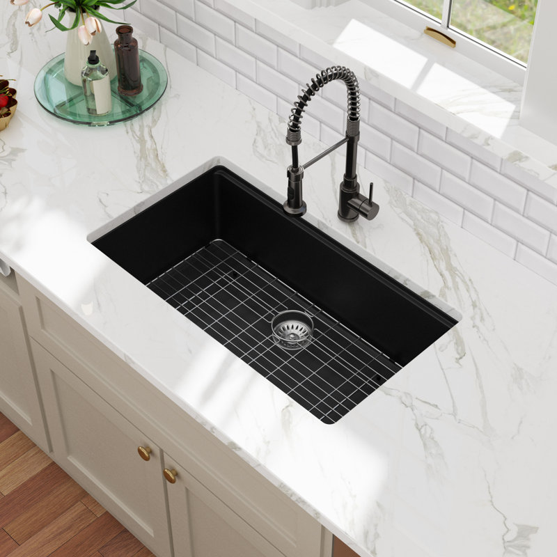 Black quartz undermount kitchen sink in a white marble countertop with a metal bottom rinse grid