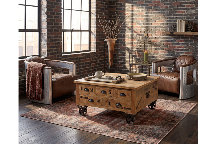 Industrial living room with brick walls, two leather-upholstered metal barrel chairs, and a refurbished wooden cart coffee table.