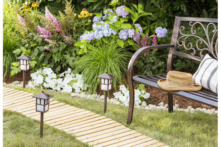 Wooden roll out walkway with solar lanterns and a bench next to a garden bed