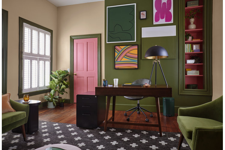 A home office with a dill green accent wall, a pink door, and green velvet chairs.