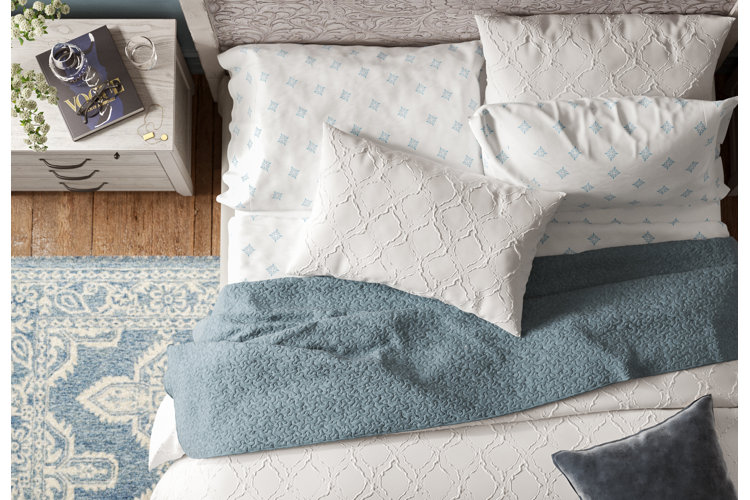 bed with white-and-blue patterned sheets, blue quilt, and a white textured duvet cover