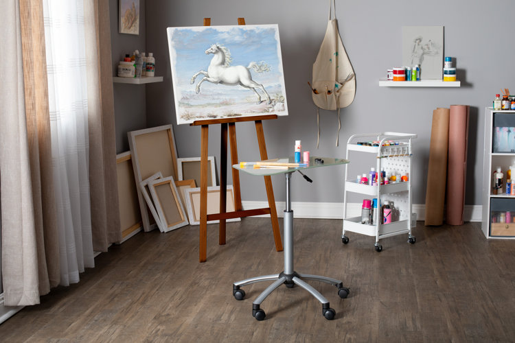 Home art studio with a bunch of art supplies and an easel used to display a painting of a horse.
